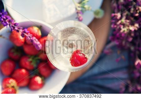 Picnic In Grass, Cheese, Strawberries, Wildflowers, Glass Of Champagne On Wooden Board.