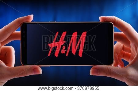 Hands Holding Smartphone Displaying Logo Of Hennes & Mauritz