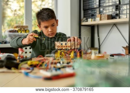 Boy Using Screwdriver While Fixing Bolts On A Robot Vehicle. Smart Kids And Stem Education. Robotics