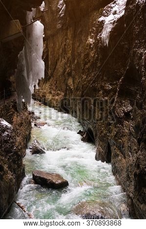 Tourists In Snow-covered Icicles At Partnachklamm, Famous Tourist Destination. Partnachklamm In Garm