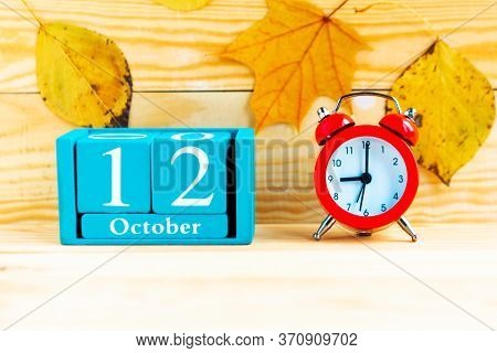 October The 12th. Blue Cube Calendar With Month And Date And Alarm Clock On Wooden Background.