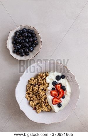 Topview Image Of Granola With Yogurt, Strawberries And Berries In A White Rustic Bowl Over Light Gra
