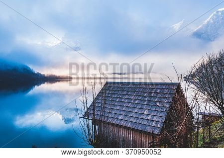 Small Wooden House On The Border Of The Lake With Foggy Mountains On The Background