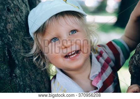 Portrait Of A Cute Happy Little Boy With Blond Hair And Blue Eyes, Whearing A Hat, Smiling And Playi