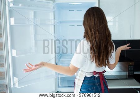 Young Woman On Kitchen During Quarantine. Look At Empty Fridge Shelves With No Food On It. Hungry An