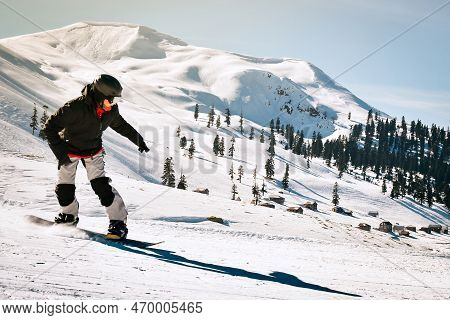 Happy Snowboarder Dressed In Dark Black Sportswear Riding Down The Mountain Slope In Georgia, Goderd