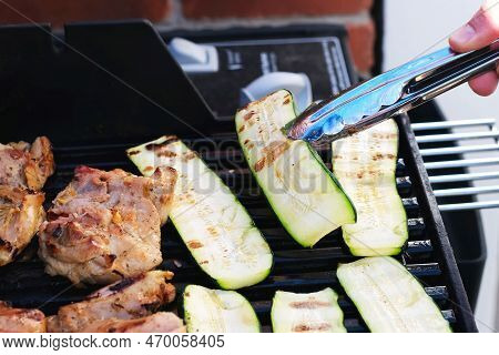 Hand Holding Piece Of Grilled Meat While Grilling Chicken And Zukini Vegetables On Outdoor Barbecue 