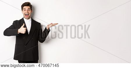 Portrait Of Hadnsome Bearded Man In Formal Suit, Showing Thumb-up And Holding Product In Hand Over W