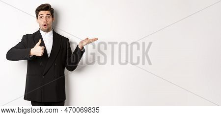 Portrait Of Hadnsome Bearded Man In Formal Suit, Showing Thumb-up And Holding Product In Hand Over W