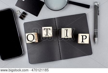 Word Qtip On A Wooden Block On A Black Notebook With Smartpone, Credit Card And Magnifier