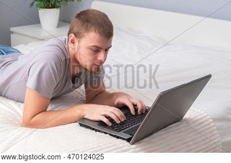 A Man With Laptop Is Lying In Bed. Freelancer Works Remotely From Home. Distance Education. Online S