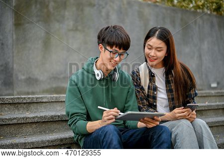 Two Cheerful Asian College Students Using Tablet On Campus Building Outdoor Stairs