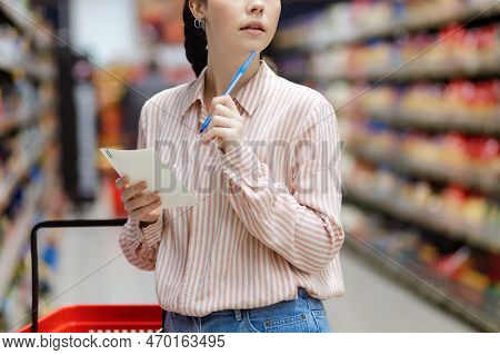 Shopping Concept. Close Up Portrait Of Young Thougtful Caucasian Woman Choosing Groceries In Superma