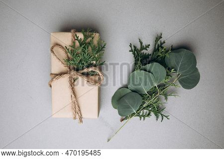 A Gift Wrapped In Brown Paper And Decorated With A Thuya Branch On A Gray Concrete Background With A