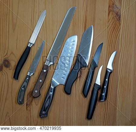 Eight Kitchen Knives On Wooden Board. The First Is A Tomato Knife, The Third A Bread Knife. Next A J