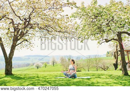 Outdoor Portrait Of Happy Young Pregnant Woman Practicing Youga In Spring Garden Under Blooming Appl