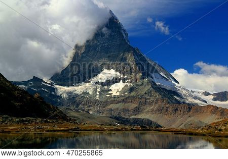 Landscape With A Mountain Matterhorn View Partially Covered By Clouds And Reflected In The Smooth Su