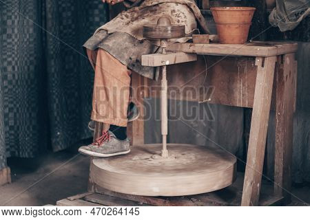 Craftsman In Dirty Working Clothes Sitting On Potter Machine. Modeling Crockery On Wheel In Pottery 