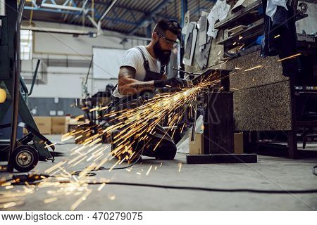 A Worker Using The Grinder For Metal Processing While Crouching In His Workshop. Small Business Work