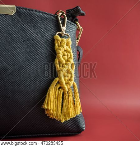 Close-up View Of The Handmade Macrame Key Chain Hanging On The Black Hand Bag Isolated On The Red Ba