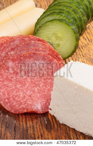 Feta und Ementhal Käse mit Salami und Gurken auf einer Holzplatte