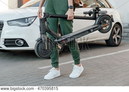 Woman Holds Folded Electric Scooter In Hands For Transportation Into Work Office