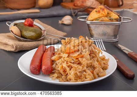 Braised Cabbage - Bigos And Smoked Sausages In A White Porcelain Plate Against The Background Of Bak