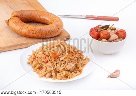 Stewed Cabbage - Bigos In A White Porcelain Plate Against The Background Of A Circle Of Smoked Sausa