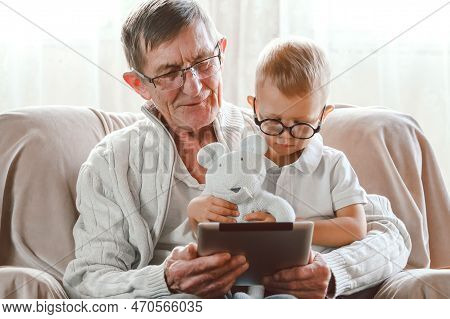 Elderly Grandfather And His Little Grandson Use A Tablet Device Together