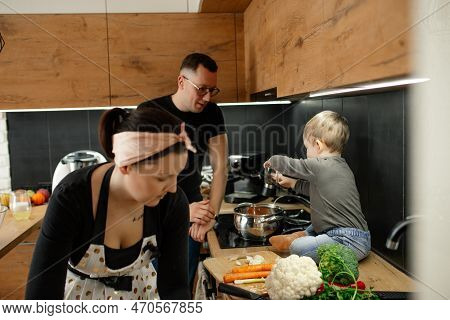 Concentrated Woman Housewife, Man, Little Blond Boy Cooking Vegetable Soup, Salad In Kitchen. Family