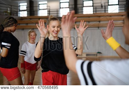 Group Of Young And Old Cheerful Women, Floorball Team Players, In Gym Cebrating Victory.