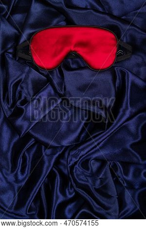 Bright Red Silk Sleep Mask Lie On Dark Blue Silken Background. Vertical Banner With Negative Space F