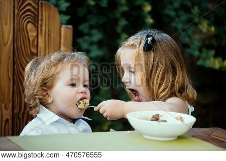 Sister Feeding Baby Boy. Girl Feeds Brother With A Spoon. Kid Food.
