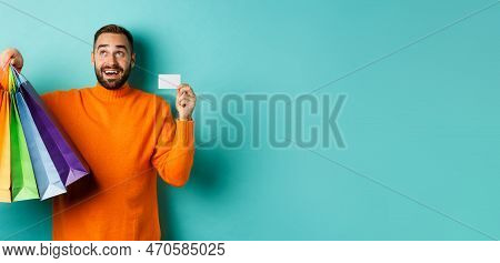 Happy Aduly Man Showing Credit Card And Shopping Bags, Standing Against Turquoise Background
