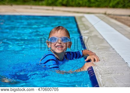 Happy Little Caucasian Boy Swims And Dives, Has Fun In The Pool In Protective Glasses. Independent C