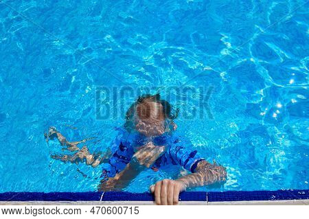 Child Clamps His Nose With His Hand And Holds His Breath, Dives In A Pool Of Warm Water. Boy Swims U