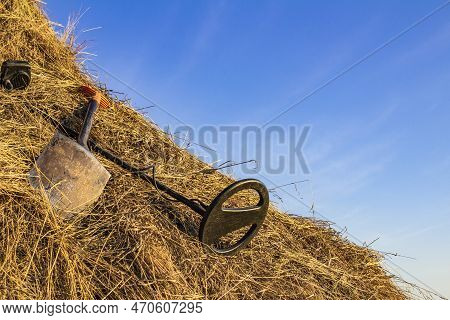 Metal Detector And Sapper Shovel On A Haystack In An Open Field Against The Blue Sky