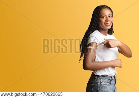 Cheerful African-american Woman With Medical Patch Aid On The Forearm After Vaccination Pointing Fin
