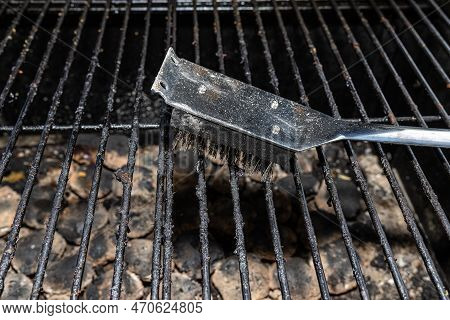 Cleaning A Dirty Grill While Standing On The Terrace And Emptying The Ashes.
