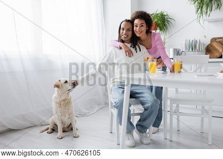 Smiling African Ameican Couple Looking At Camera Near Breakfast And Labrador At Home.