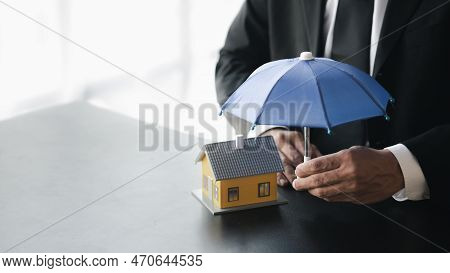 Individuals Holding Small Umbrellas And Model Homes, Housing Insurance Against Impending Loss And Fi