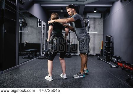 A Young Male Personal Trainer Assists A Woman In An Electric Muscle Suit To Stimulate Muscles. Fitne