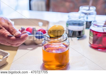 Old Woman Dyeing Easter Eggs At Home In The Kitchen In The Cucumber Glass And With Different Colors,