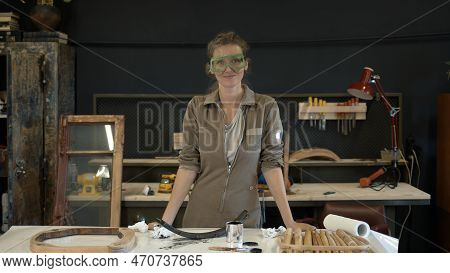 Woman Putting On Safety Glasses, Middle Shot In The Workshop. Young Woman In Worksuit Put On Goggles