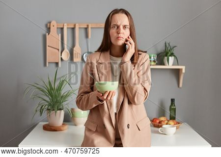 Photo Of Astonished Sad Upset Brown Haired Woman Wearing Beige Suit Standing Near Table On Kitchen A