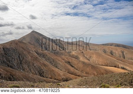 Shapes And Lines Of The Mountains Of The Volcanic Origin. Light Brown Color Of The Soil. Sky With Cl