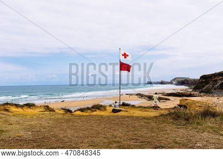 Liencres, Spain- August 14, 2022: Beach Of Liencres. Rescue Red Cross Flag And Red Flag Waving In Th
