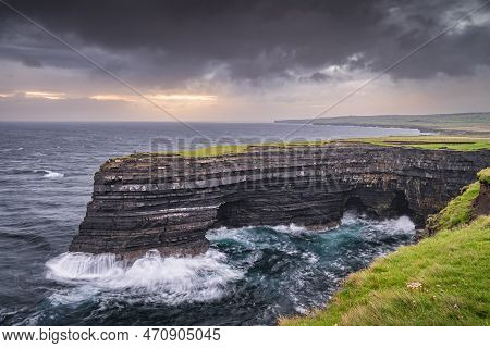 Lonely Fisherman Standing On The Edge Of Downpatrick Head Cliffs With Crashing Waves Beneath At Dawn