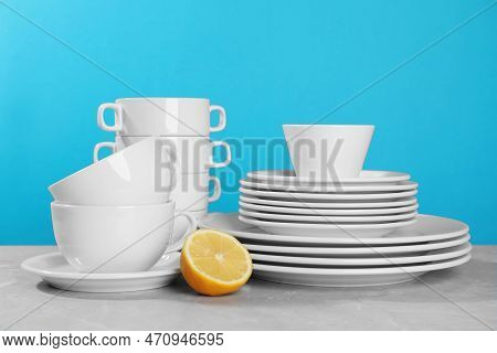 Clean Tableware And Half Of Lemon On Grey Table Against Light Blue Background