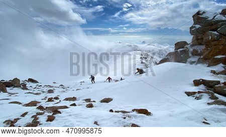 Several Hikers Climb Uphill In A Heavy Snowstorm. Climbers With Small Backpacks And Trekking Poles W